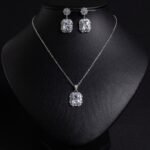 Niche emerald cut crystal jewelry set wholesale featuring a radiant halo CZ rectangular crystal pendant chain necklace and matching drop earrings from junejewelry.com
