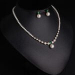 Niche small pearl necklace jewelry set wholesale featuring delicate round faux pearls, an emerald-green cubic zirconia center accent, and matching pearl stud earrings from junejewelry.com