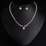 Niche small pearl necklace jewelry set wholesale featuring delicate round faux pearls, an emerald-green cubic zirconia center accent, and matching pearl stud earrings from junejewelry.com