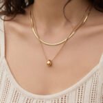 Model wearing double layer gold teardrop pendant necklace with flat snake chain