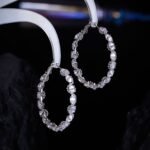 Cubic zirconia oval hoop earrings featuring continuous prong-set round stones, available in gold and silver tones in two sizes.