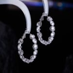 Cubic zirconia oval hoop earrings featuring continuous prong-set round stones, available in gold and silver tones in two sizes.