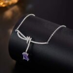 Niche purple zircon bow ribbon necklace earring set wholesale featuring a paved ribbon bow pendant suspending a rectangular emerald-cut purple zircon stone, paired with matching purple stud earrings from junejewelry.com