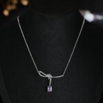 Niche purple zircon bow ribbon necklace earring set wholesale featuring a paved ribbon bow pendant suspending a rectangular emerald-cut purple zircon stone, paired with matching purple stud earrings from junejewelry.com