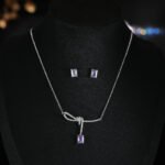 Niche purple zircon bow ribbon necklace earring set wholesale featuring a paved ribbon bow pendant suspending a rectangular emerald-cut purple zircon stone, paired with matching purple stud earrings from junejewelry.com