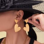 Stainless steel gold heart jewelry set featuring a long station sweater necklace, double heart drop earrings, and a large heart statement ring.