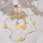Stainless steel gold heart jewelry set featuring a long station sweater necklace, double heart drop earrings, and a large heart statement ring.