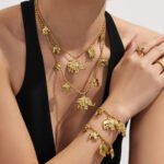 18K gold plated stainless steel elephant charm necklace and bracelet set featuring a prominent central elephant pendant and smaller charm accents on a beaded ball chain.