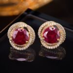 Round ruby stud earrings wholesale featuring a vibrant red central CZ stone wrapped in a swirling pavé cubic zirconia halo with S925 sterling silver posts from junejewelry.com