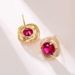 Round ruby stud earrings wholesale featuring a vibrant red central CZ stone wrapped in a swirling pavé cubic zirconia halo with S925 sterling silver posts from junejewelry.com