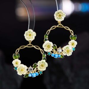 Twisted round hoop earrings adorned with hand-painted enamel flowers, green leaves, and CZ crystal accents in purple and white options.