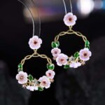Twisted round hoop earrings adorned with hand-painted enamel flowers, green leaves, and CZ crystal accents in purple and white options.