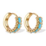 Small beaded huggie hoop earrings set with baguette-cut turquoise stones and flanked by textured metal beads in gold and silver plating options.