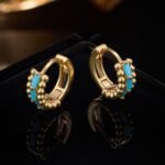 Small beaded huggie hoop earrings set with baguette-cut turquoise stones and flanked by textured metal beads in gold and silver plating options.