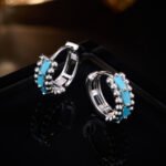 Small beaded huggie hoop earrings set with baguette-cut turquoise stones and flanked by textured metal beads in gold and silver plating options.