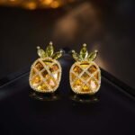 Sparkling pineapple stud earrings featuring marquise-cut crystal crown leaves, lattice fruit body, and micro-pavé accents in yellow, pink, and clear options.