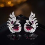 Sculpted peacock-shaped stud earrings set with vibrant pear-cut cubic zirconia stones and pavé feather details, available in emerald green, rose pink, and sapphire blue options.