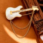 Cool rock style natural mother of pearl guitar brooch pin wholesale featuring 18K real gold plated copper, baguette CZ neck, and draped chain tassels from junejewelry.com