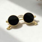 Sunglasses brooch wholesale featuring round black lenses, gold-plated wire frame, and cubic zirconia paved bridge accent from junejewelry.com