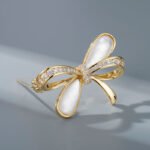 Delicate bow knot shell brooch wholesale featuring pavé cubic zirconia ribbons, inlaid natural mother of pearl shell loops, and a gold-plated finish from junejewelry.com