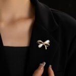 Delicate bow knot shell brooch wholesale featuring pavé cubic zirconia ribbons, inlaid natural mother of pearl shell loops, and a gold-plated finish from junejewelry.com