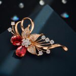 Dazzling rose gold flower brooch wholesale featuring micro-pave cubic zirconia petals, round crystal accents, and pear-cut red crystal gems from junejewelry.com