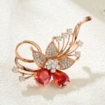 Dazzling rose gold flower brooch wholesale featuring micro-pave cubic zirconia petals, round crystal accents, and pear-cut red crystal gems from junejewelry.com