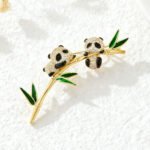 Panda bamboo brooch wholesale featuring two pavé cubic zirconia pandas clinging to a gold-plated bamboo stalk with green enamel leaves from junejewelry.com