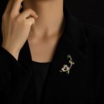 Double panda brooch wholesale featuring a micro-pavé cubic zirconia mother panda and smooth baby panda playing on a curved gold bamboo stalk with green enamel leaves from junejewelry.com