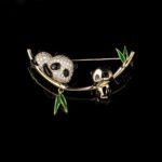 Double panda brooch wholesale featuring a micro-pavé cubic zirconia mother panda and smooth baby panda playing on a curved gold bamboo stalk with green enamel leaves from junejewelry.com