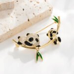 Double panda brooch wholesale featuring a micro-pavé cubic zirconia mother panda and smooth baby panda playing on a curved gold bamboo stalk with green enamel leaves from junejewelry.com