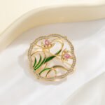 Orchid brooch wholesale featuring a circular micro-pavé frame enclosing pink enamel orchid blossoms and green enamel leaves in gold plating from junejewelry.com