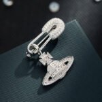 Trendy planet safety pin brooch wholesale featuring a pavé cubic zirconia encrusted safety pin header with a dangling crystal Saturn orb pendant from junejewelry.com