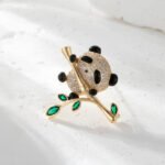 Panda brooch wholesale featuring micro-pavé cubic zirconia panda hugging a gold bamboo stalk with marquise emerald green crystal leaves from junejewelry.com