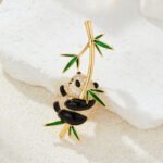 Playful Chinese style hanging panda bamboo CZ brooch wholesale featuring a chubby micro-pave cubic zirconia panda clinging to a gold-plated bamboo stalk with vibrant green enamel leaves from junejewelry.com