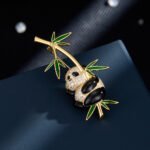 Playful Chinese style hanging panda bamboo CZ brooch wholesale featuring a chubby micro-pave cubic zirconia panda clinging to a gold-plated bamboo stalk with vibrant green enamel leaves from junejewelry.com