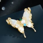 Pearl shell butterfly brooch wholesale featuring natural mother-of-pearl wings overlaid with pavé CZ vine tendrils, a center faux pearl, and multi-color cubic zirconia accents from junejewelry.com