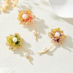 Oriental luxury Chinese style enamel lotus pearl brooch wholesale featuring translucent enamel petals, yellow enamel stamens, micro-pave CZ outlines, and dual freshwater pearls on a gold stem from junejewelry.com