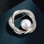 Geometric round pearl brooch wholesale featuring interlocking polished metal and micro-pavé cubic zirconia swirl rings framing a round center pearl from junejewelry.com
