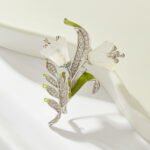 Light luxury white agate lily of the valley brooch wholesale featuring carved translucent white agate bell-shaped blooms, fresh green enamel leaves, and micro-pave cubic zirconia foliage on a silver setting from junejewelry.com