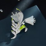 Light luxury white agate lily of the valley brooch wholesale featuring carved translucent white agate bell-shaped blooms, fresh green enamel leaves, and micro-pave cubic zirconia foliage on a silver setting from junejewelry.com