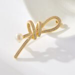 Elegant micro pave ribbon pearl brooch wholesale featuring a sparkling cubic zirconia encrusted looped ribbon bow knot tipped with a lustrous white pearl from junejewelry.com
