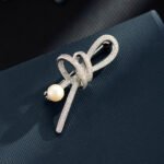 Elegant micro pave ribbon pearl brooch wholesale featuring a sparkling cubic zirconia encrusted looped ribbon bow knot tipped with a lustrous white pearl from junejewelry.com