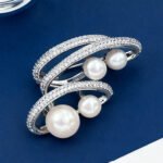 Light luxury layered pearl cluster brooch wholesale featuring multi-tiered micro-pave cubic zirconia curved bands nestled with lustrous white pearls from junejewelry.com