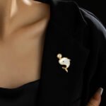 Playful cute mother of pearl whale brooch wholesale featuring a smooth iridescent white shell body, black gem eye, and round pearl water spout in gold or silver trim from junejewelry.com