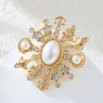 Light luxury unisex nautical pearl star anchor CZ brooch wholesale featuring a large oval pearl centerpiece framed by a starburst of anchors, sea shells, star-cut crystals, and paved cubic zirconia in gold or silver finish from junejewelry.com