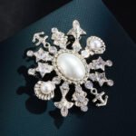 Light luxury unisex nautical pearl star anchor CZ brooch wholesale featuring a large oval pearl centerpiece framed by a starburst of anchors, sea shells, star-cut crystals, and paved cubic zirconia in gold or silver finish from junejewelry.com