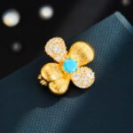 Four petal flower brooch wholesale featuring two brushed gold finish petals, two pavé cubic zirconia petals, and a turquoise stone center in gold plating from junejewelry.com