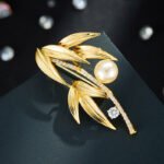 Elegant bamboo leaf pearl brooch wholesale featuring textured metallic leaves, a pavé cubic zirconia curved bamboo stalk, a sparkling solitaire round CZ accent, and a glossy pearl drop from junejewelry.com