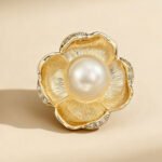 Pearl flower brooch wholesale featuring five brushed gold textured petals trimmed with micro-pavé cubic zirconia and a large center faux pearl from junejewelry.com